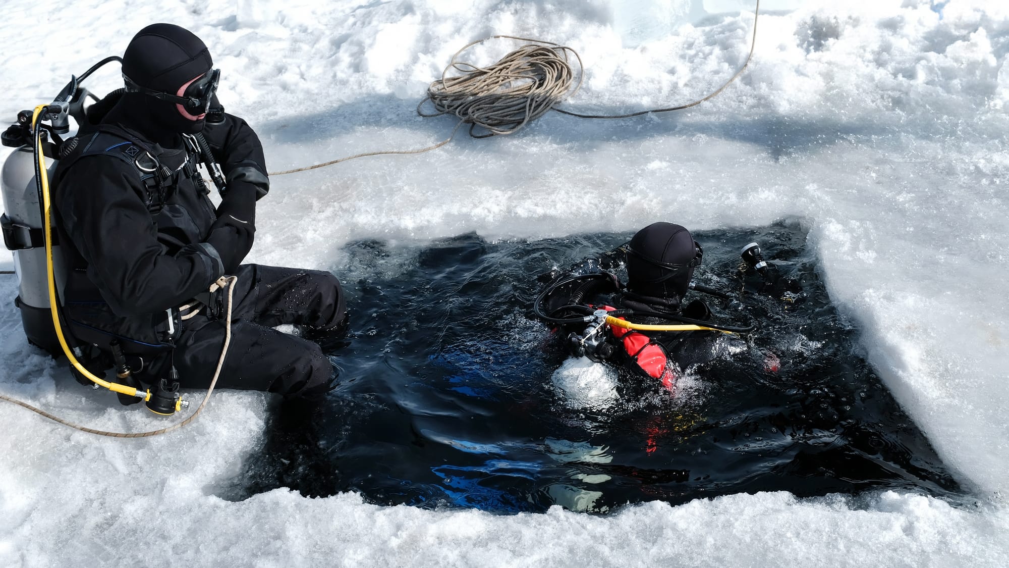 Scuba diver using drysuits preparing to dive beneath a layer of ice.