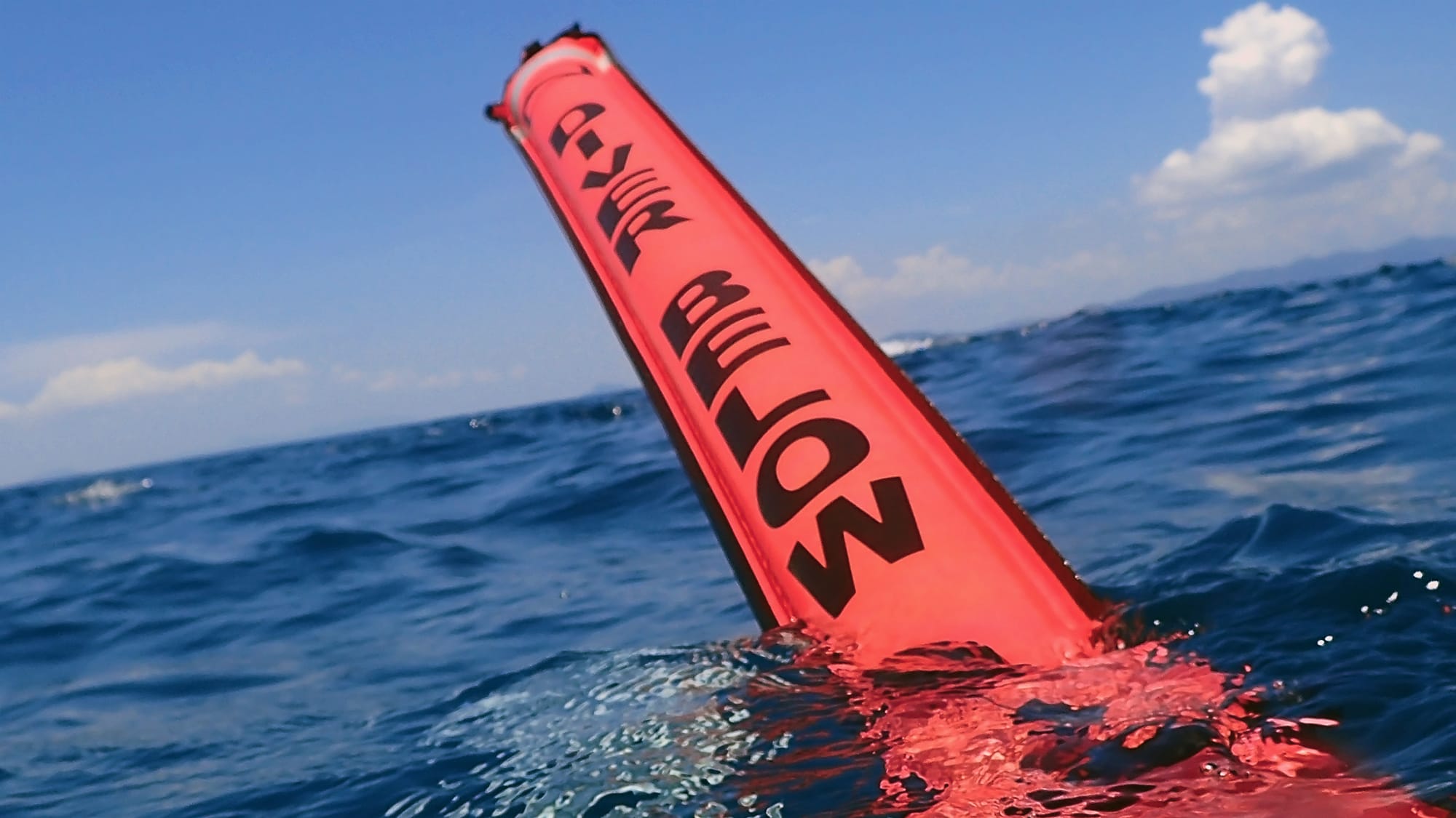 An orange Surface Marker Buoy being deployed on the surface, reading "diver below"