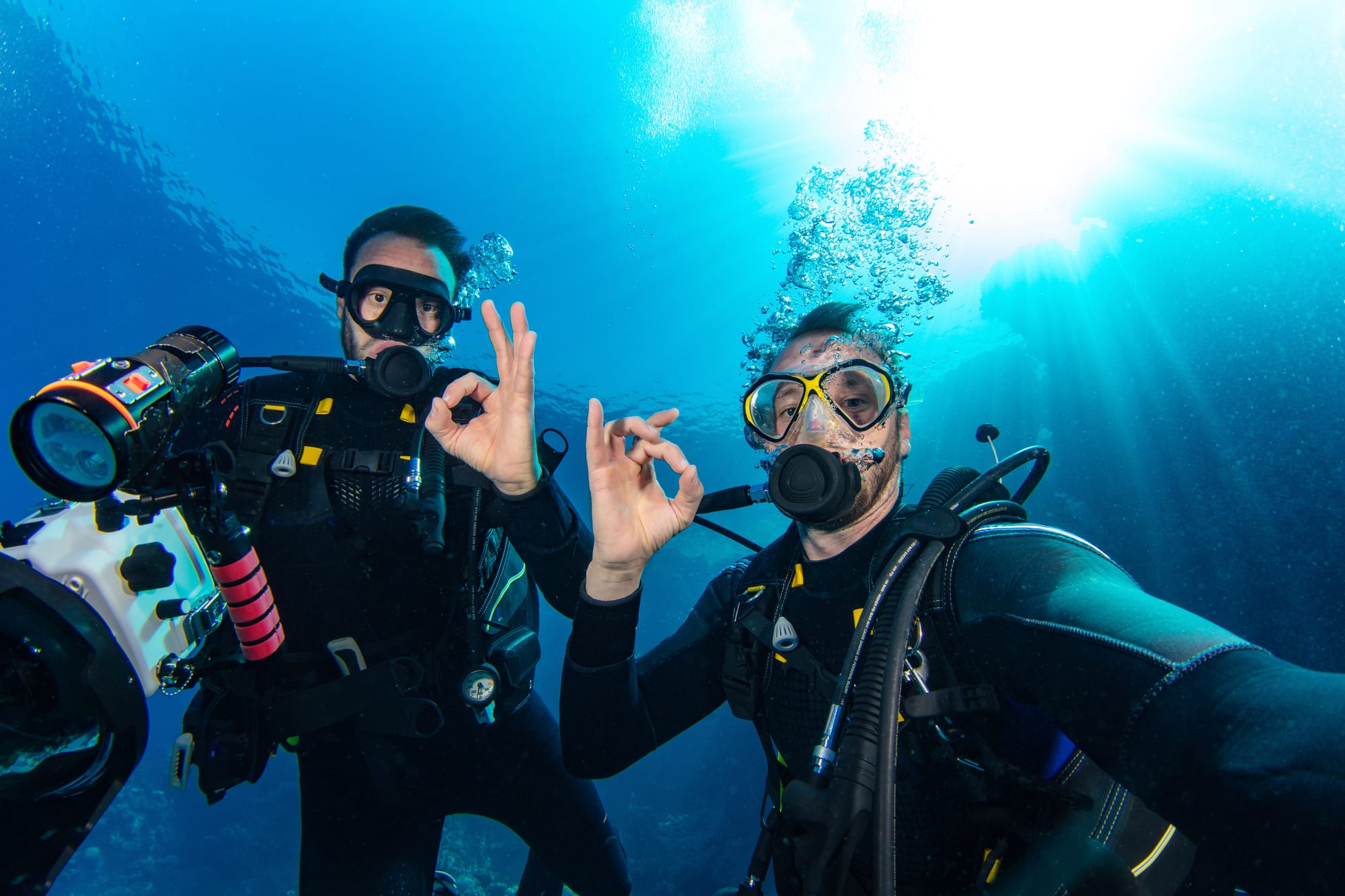 Scuba divers underwater looking at the camera and flashing an ok sign