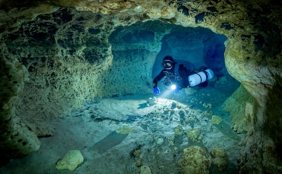 Cave diver in a cave, yellow walls illuminated by the torch